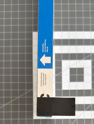 Applying the tape to the corner of the filter. Note the airflow direction on the filter and make sure the tab is sticking out toward the front of the filter.